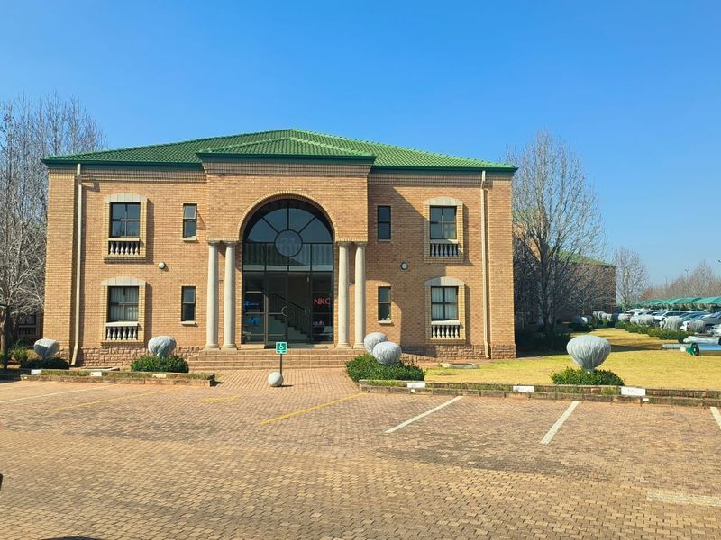 Front elevation of a two-story brick office building featuring an arched entrance, columns, and a paved parking area.