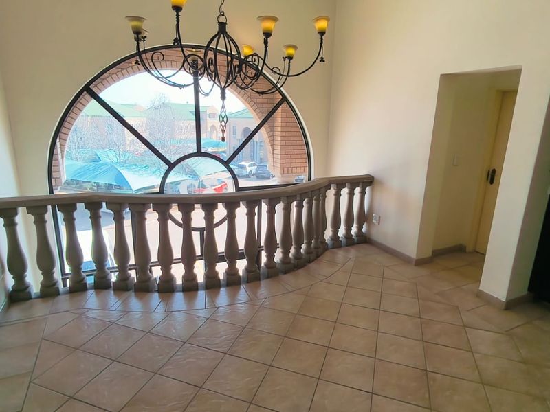 Spacious entrance foyer featuring a large arched window, decorative stone balustrade, and elegant wrought iron chandelier with neutral tiled flooring.