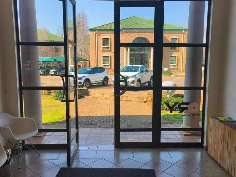 Bright office entrance featuring large glass doors, tiled flooring, and structural columns, providing a clear view of the exterior parking area.