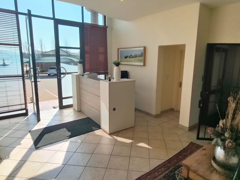 Bright office entrance featuring large glass windows, tiled flooring, and a professional built-in reception desk area.