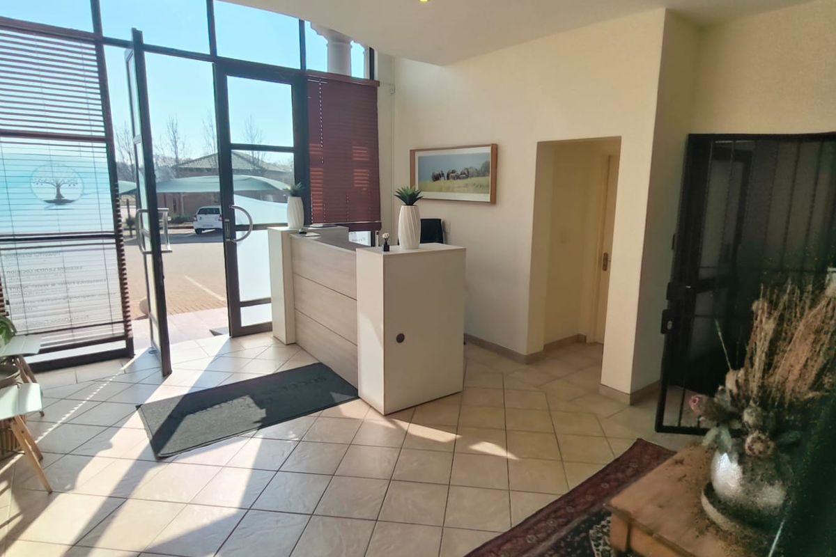Bright office entrance featuring large glass windows, tiled flooring, and a professional built-in reception desk area.