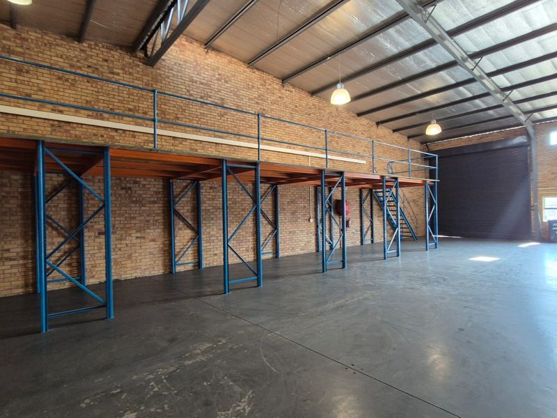 Spacious industrial warehouse unit featuring a large mezzanine storage level, high ceilings, concrete flooring, and a secure roller shutter door for easy access.