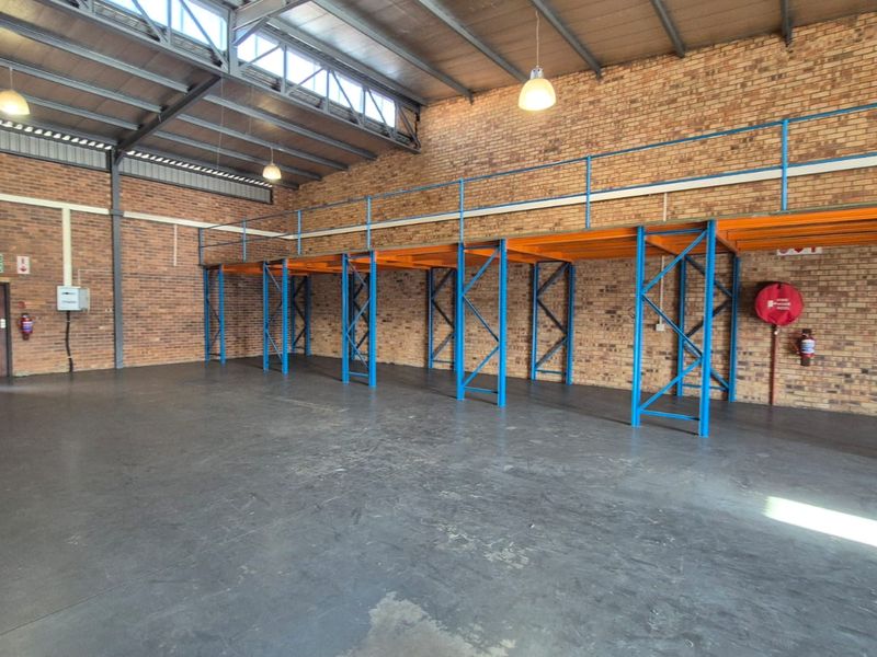 Spacious industrial warehouse unit featuring exposed brick walls, durable concrete flooring, high-bay lighting, and integrated steel mezzanine racking for efficient storage.