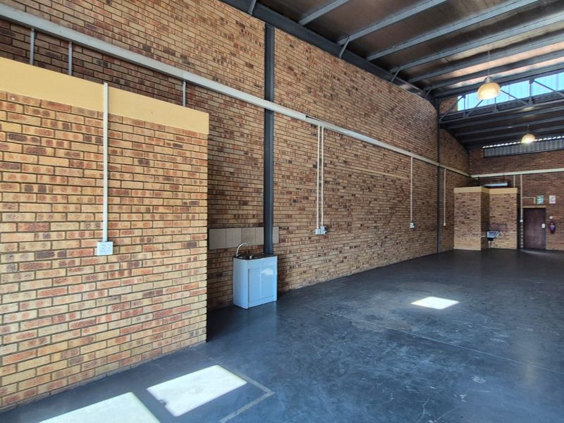 Spacious industrial utility area featuring exposed brick walls, high steel roof trusses, concrete flooring, and a functional utility sink.