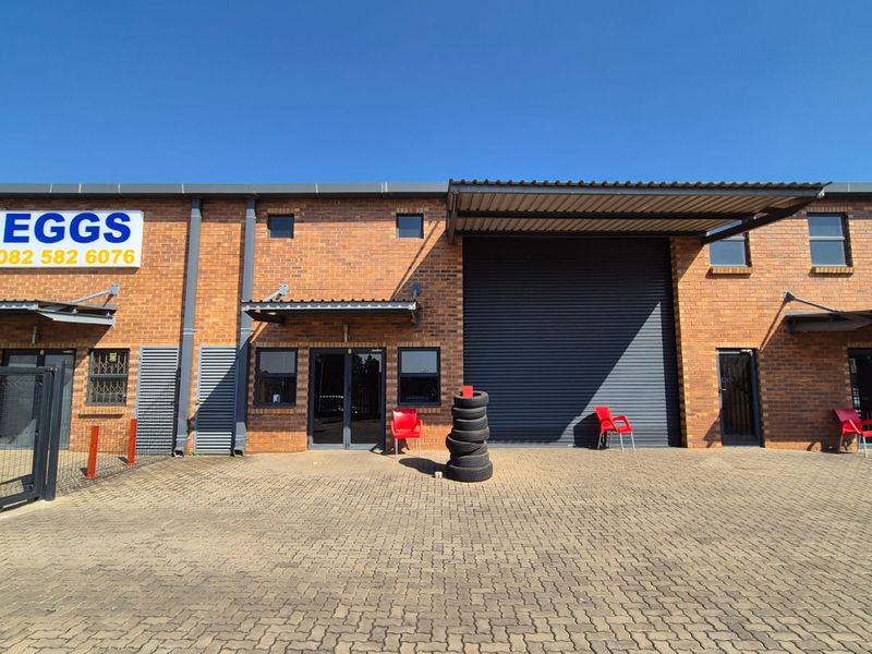 Front elevation of an industrial unit featuring a brick facade, roller shutter door, paved driveway, and metal awnings for loading access.