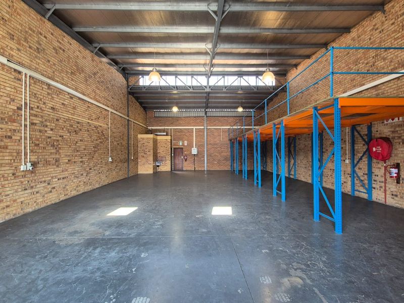 Spacious industrial warehouse unit featuring exposed brick walls, high ceilings with steel trusses, concrete flooring, and a built-in steel mezzanine storage level.