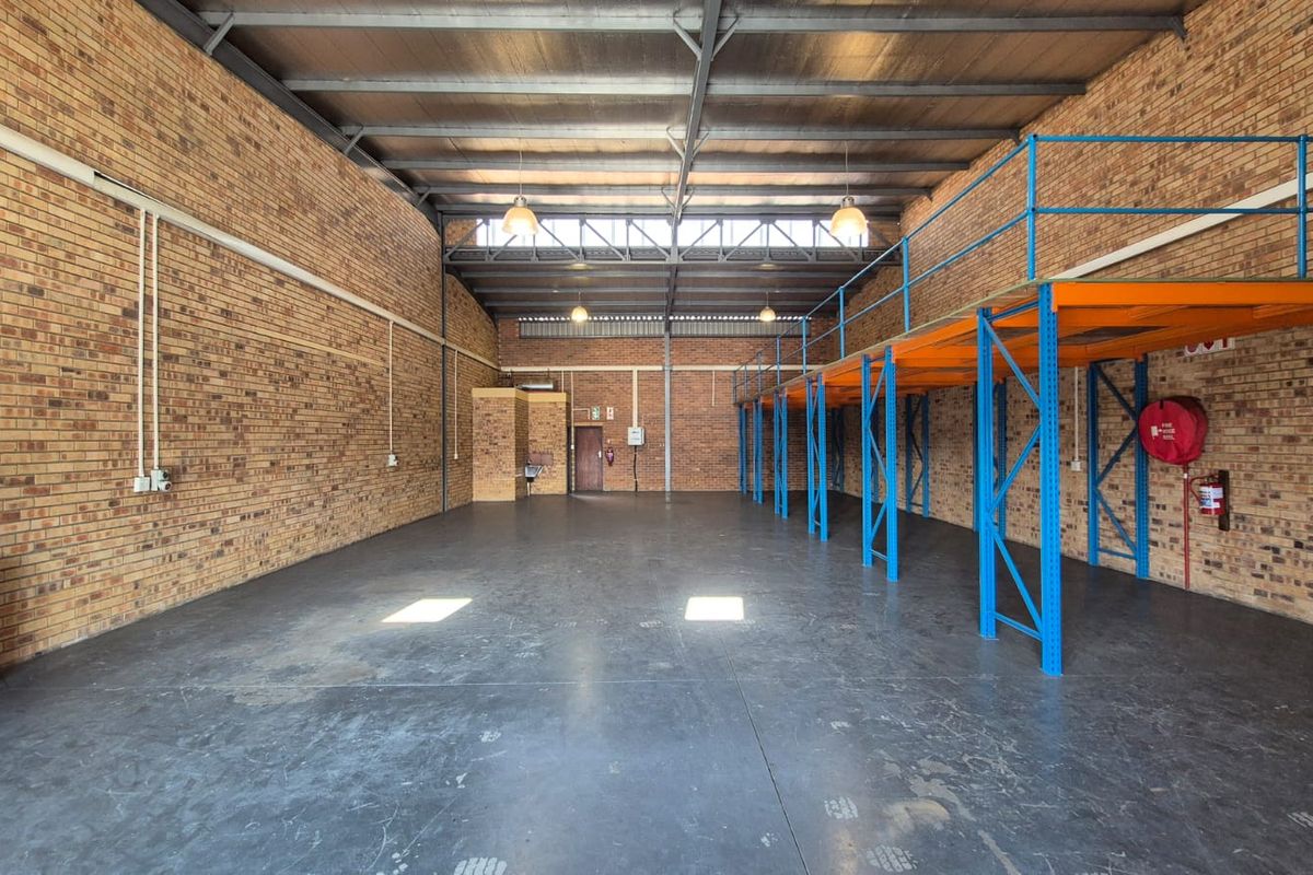 Spacious industrial warehouse unit featuring exposed brick walls, high ceilings with steel trusses, concrete flooring, and a built-in steel mezzanine storage level.