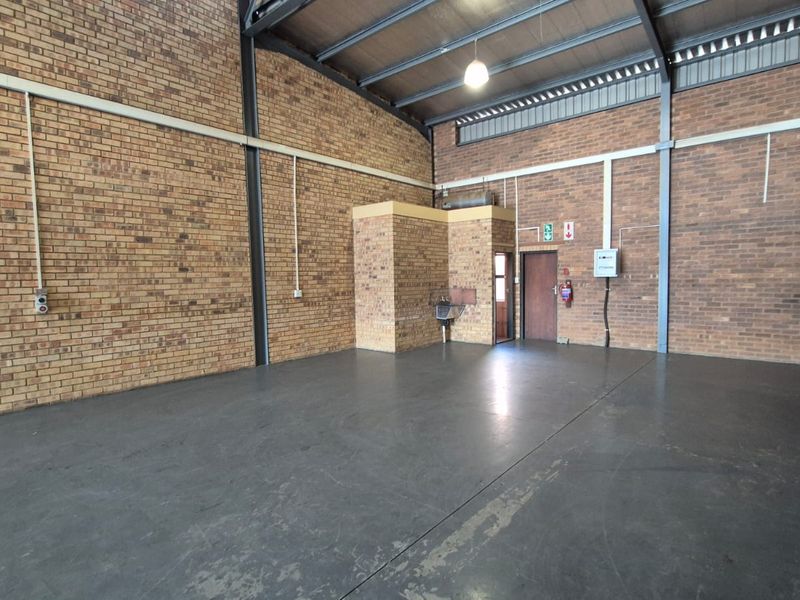 Spacious industrial utility area featuring exposed brick walls, concrete flooring, high steel roof trusses, and a mezzanine level, suitable for storage or workshop use.