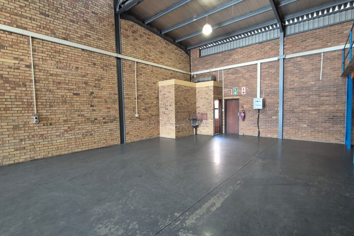 Spacious industrial utility area featuring exposed brick walls, concrete flooring, high steel roof trusses, and a mezzanine level, suitable for storage or workshop use.