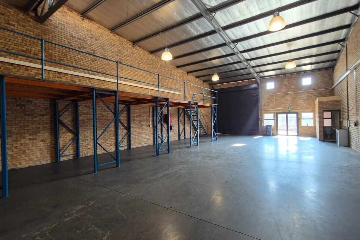 Spacious industrial warehouse unit featuring high ceilings, exposed brick walls, a functional steel mezzanine level, and a large roller shutter door for easy access.