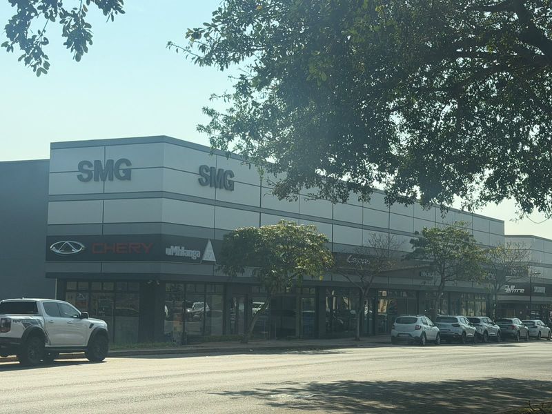 Street-level view of a modern commercial retail building featuring metal cladding, large glass storefronts, and prominent business signage.
