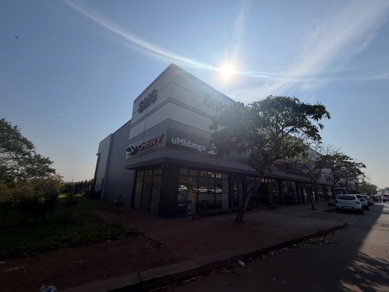 A modern commercial retail building featuring a prominent glass storefront, professional signage, and paved street-level access.