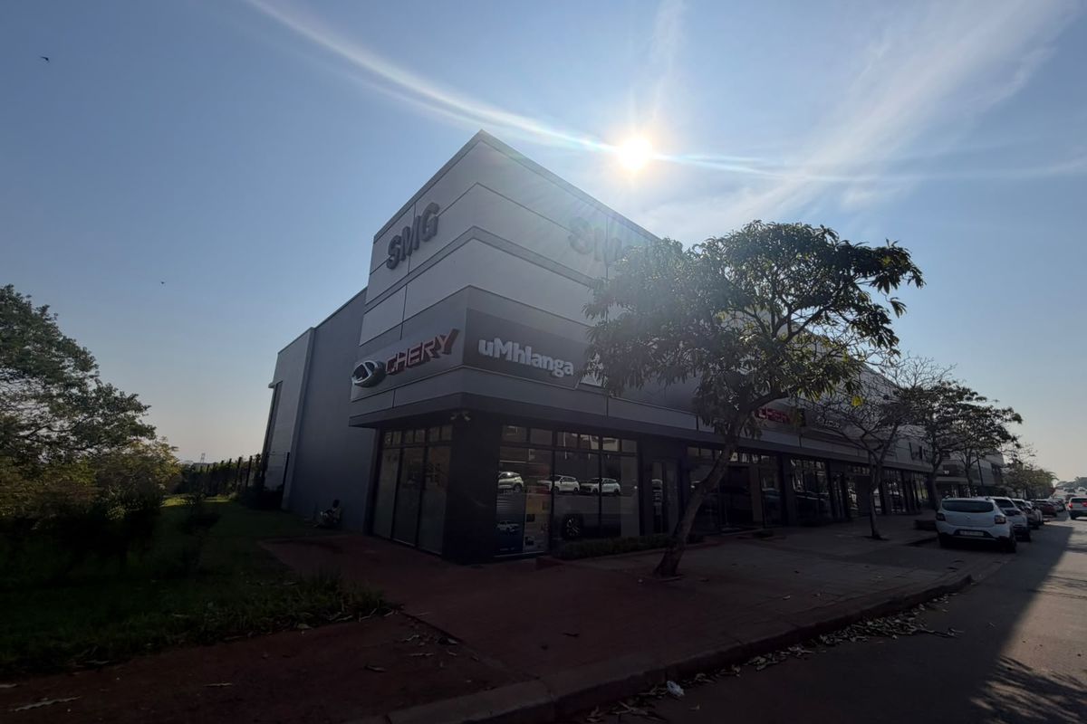A modern commercial retail building featuring a prominent glass storefront, professional signage, and paved street-level access.