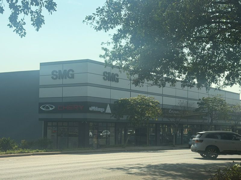 Front exterior view of a modern commercial retail building featuring metal cladding, prominent signage, and large glass storefront windows.