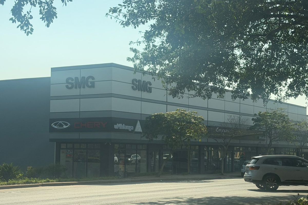 Front exterior view of a modern commercial retail building featuring metal cladding, prominent signage, and large glass storefront windows.