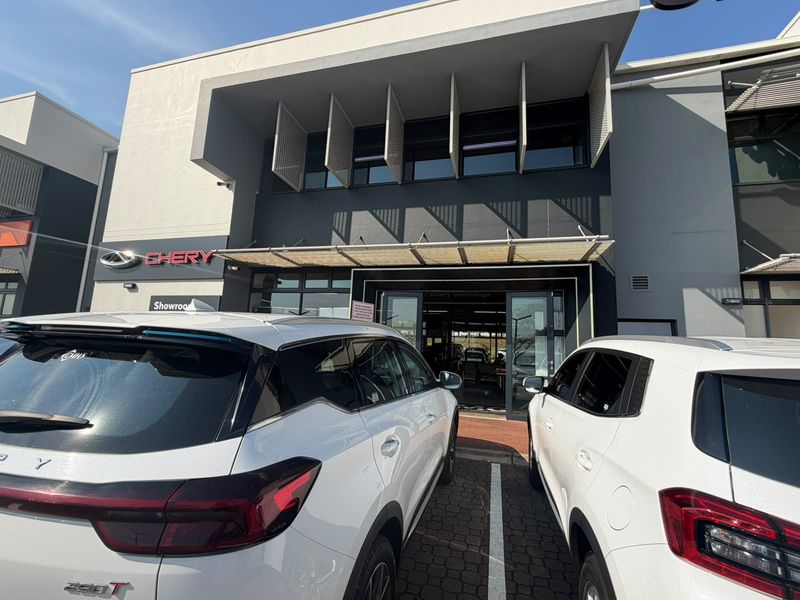 Modern commercial showroom exterior featuring a contemporary facade with architectural sun louvers and glass entrance doors, situated in a paved parking area.