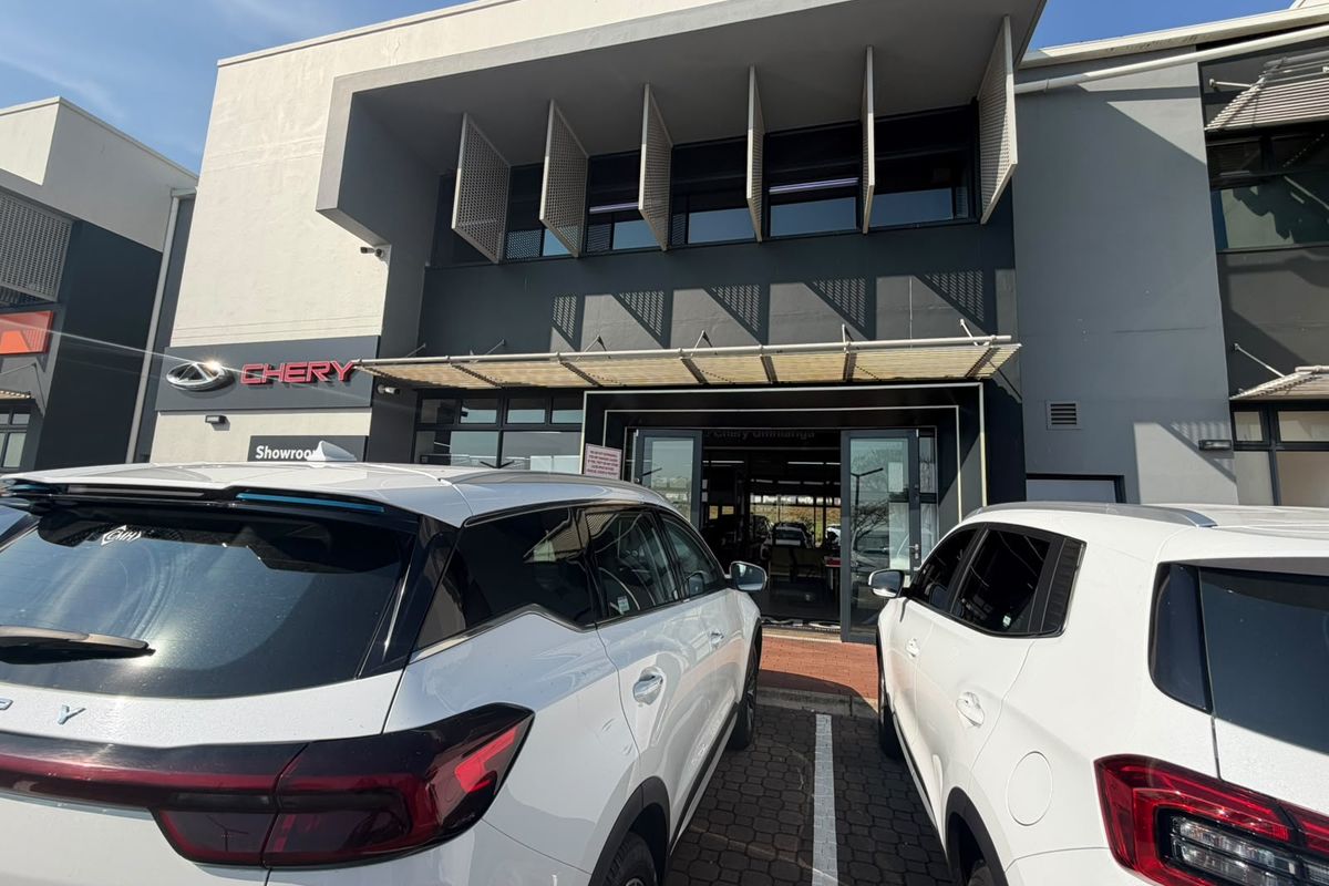 Modern commercial showroom exterior featuring a contemporary facade with architectural sun louvers and glass entrance doors, situated in a paved parking area.