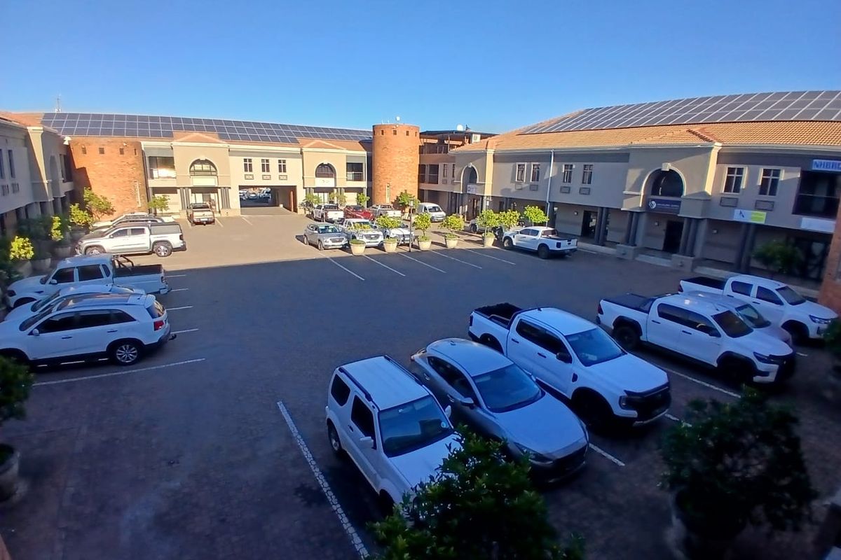 Aerial view of a commercial office complex courtyard featuring paved parking, brick architecture, and roof-mounted solar panels.