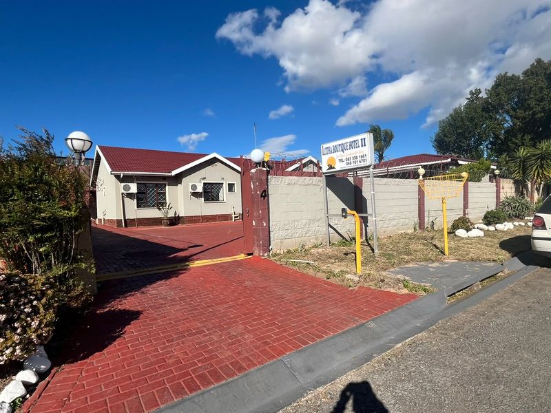 Front exterior view of the guest house featuring a paved driveway, secure perimeter wall with razor wire, and prominent business signage.
