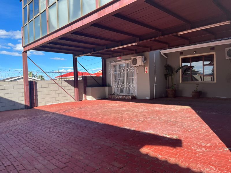 A covered entrance area featuring a paved driveway, security gate, and exterior air conditioning unit, serving as a functional reception access point.