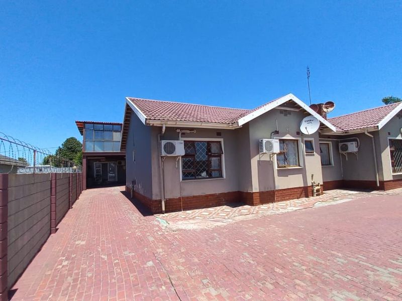 Front exterior view of the guest house featuring a paved driveway, perimeter wall with security fencing, and multiple wall-mounted air conditioning units.