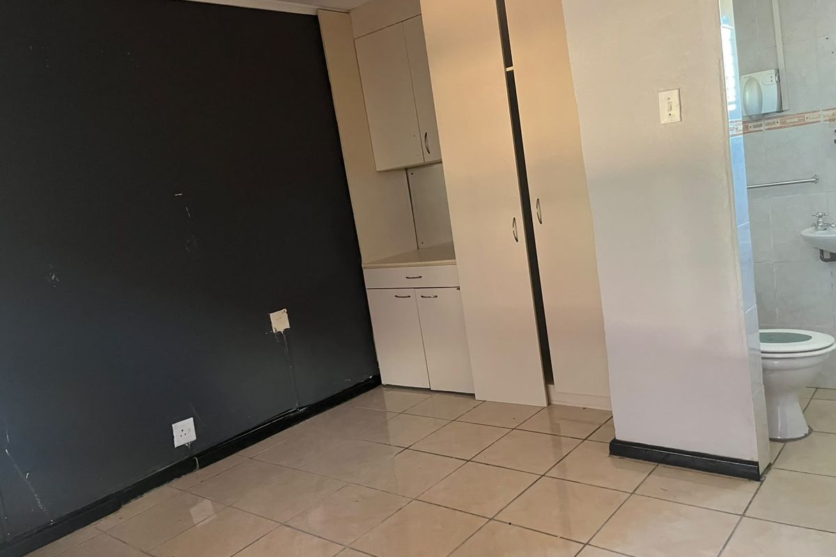 An empty bedroom featuring tiled flooring, built-in cupboards, and an attached en-suite bathroom with a toilet and basin.