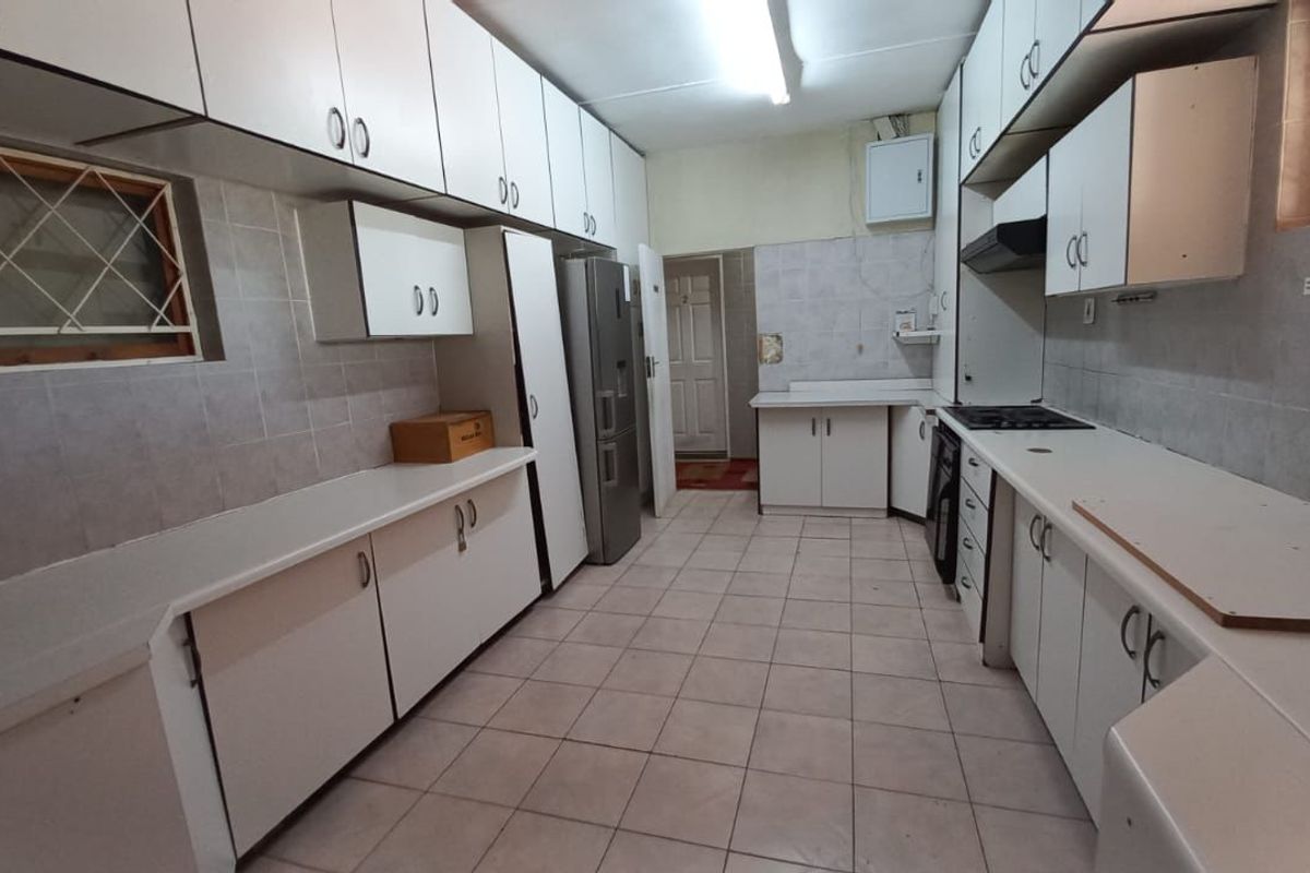 A functional kitchen featuring extensive built-in cabinetry, tiled surfaces, and integrated cooking appliances, offering a practical layout for a guest house environment.
