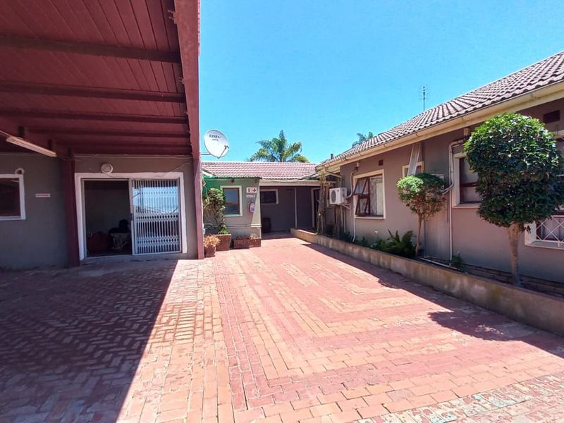 A paved rear courtyard area featuring a covered carport, multiple building access points, and exterior wall finishes with integrated air conditioning units.