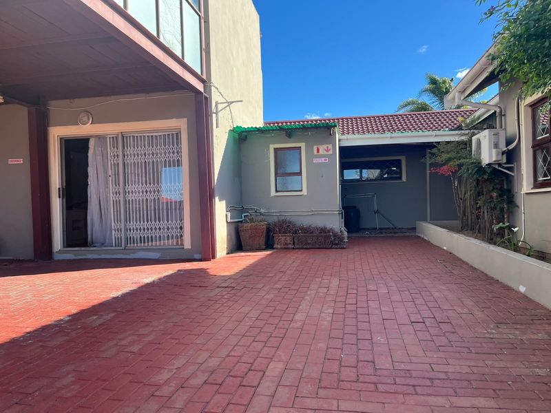 Exterior view of a guest house courtyard featuring a paved driveway, sliding door access, and external air conditioning unit.