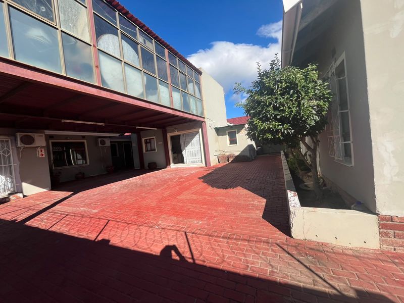 A paved rear courtyard area featuring a covered parking structure, raised planter box, and exterior access points to the guest house.