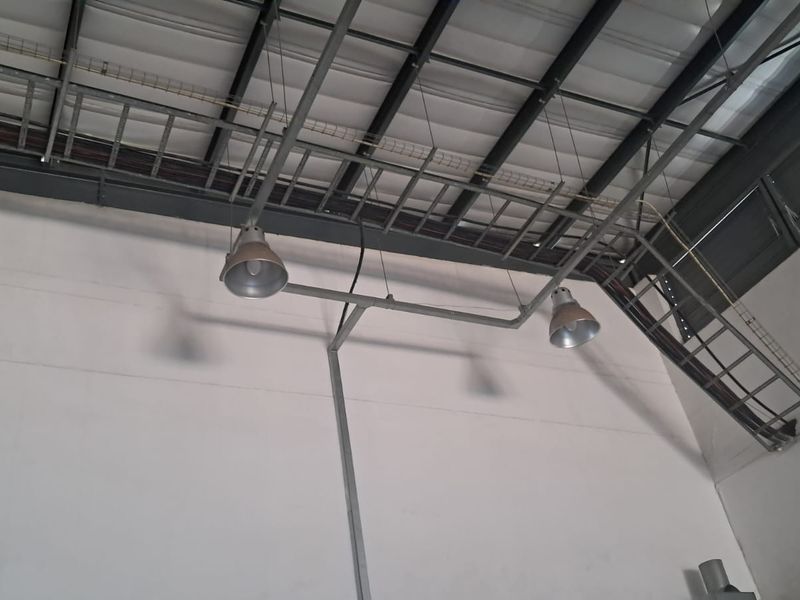Interior view of an industrial utility space featuring exposed steel roof trusses, cable management systems, and industrial pendant lighting fixtures.