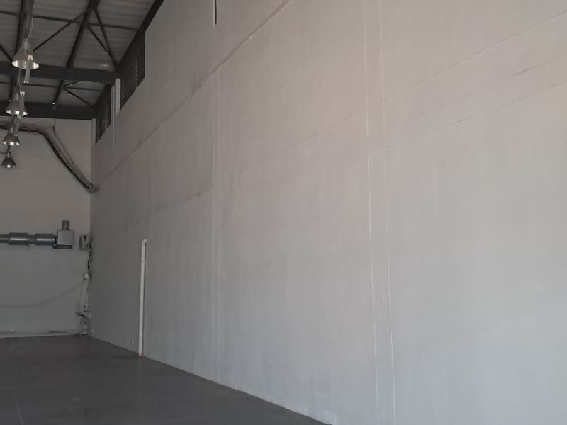 Spacious industrial utility area featuring high ceilings with exposed steel trusses, concrete flooring, and functional industrial lighting.