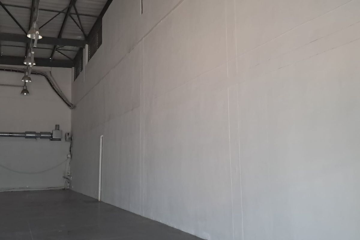 Spacious industrial utility area featuring high ceilings with exposed steel trusses, concrete flooring, and functional industrial lighting.