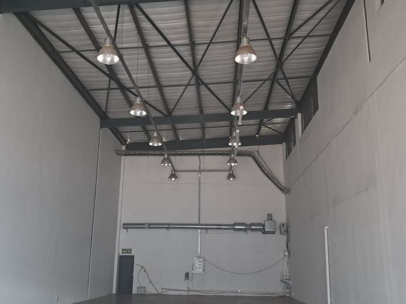 Spacious industrial utility area featuring high ceilings with exposed steel trusses, industrial pendant lighting, and functional ventilation ducting.