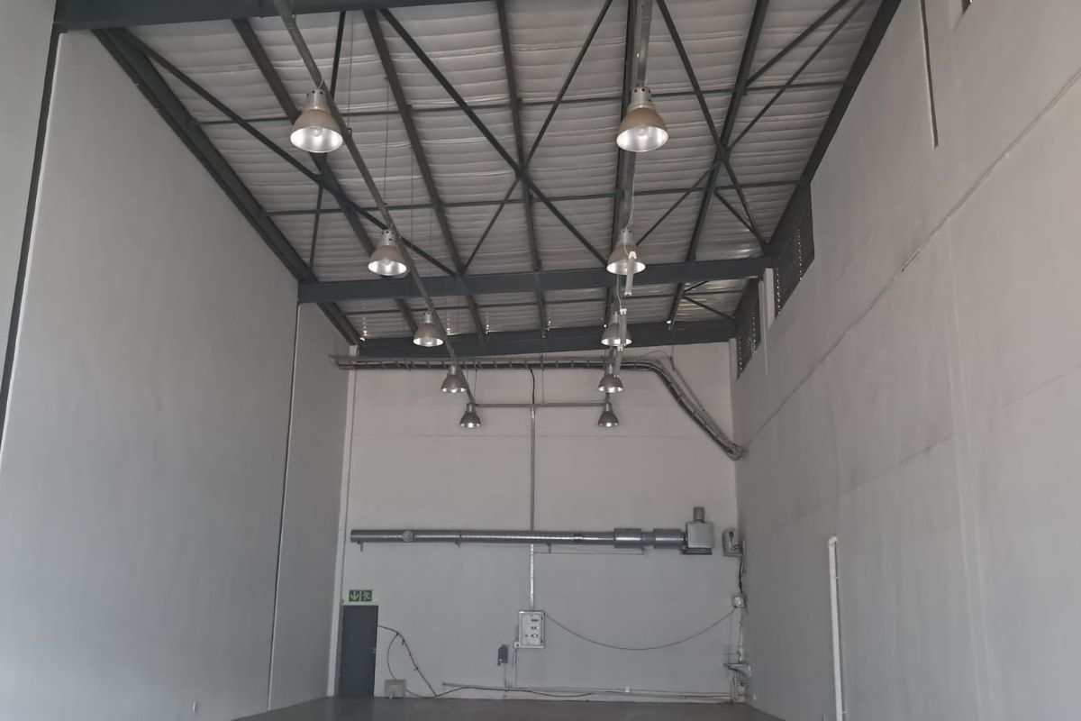 Spacious industrial utility area featuring high ceilings with exposed steel trusses, industrial pendant lighting, and functional ventilation ducting.