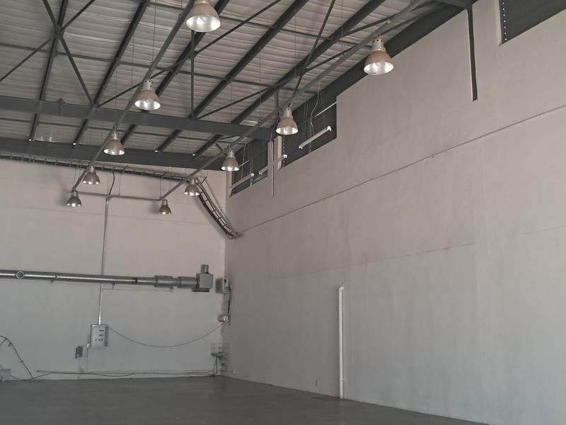 Spacious industrial warehouse unit featuring high ceilings with exposed steel trusses, industrial pendant lighting, and durable concrete flooring.