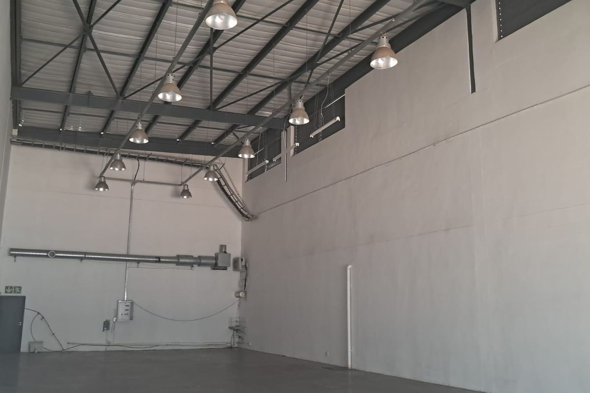 Spacious industrial warehouse unit featuring high ceilings with exposed steel trusses, industrial pendant lighting, and durable concrete flooring.