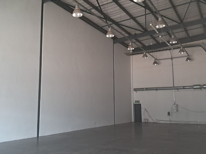 Spacious industrial warehouse unit featuring high ceilings with exposed steel trusses, polished concrete flooring, and functional industrial lighting throughout.