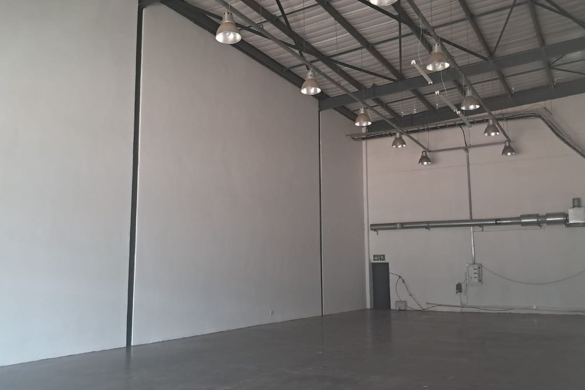 Spacious industrial warehouse unit featuring high ceilings with exposed steel trusses, polished concrete flooring, and functional industrial lighting throughout.