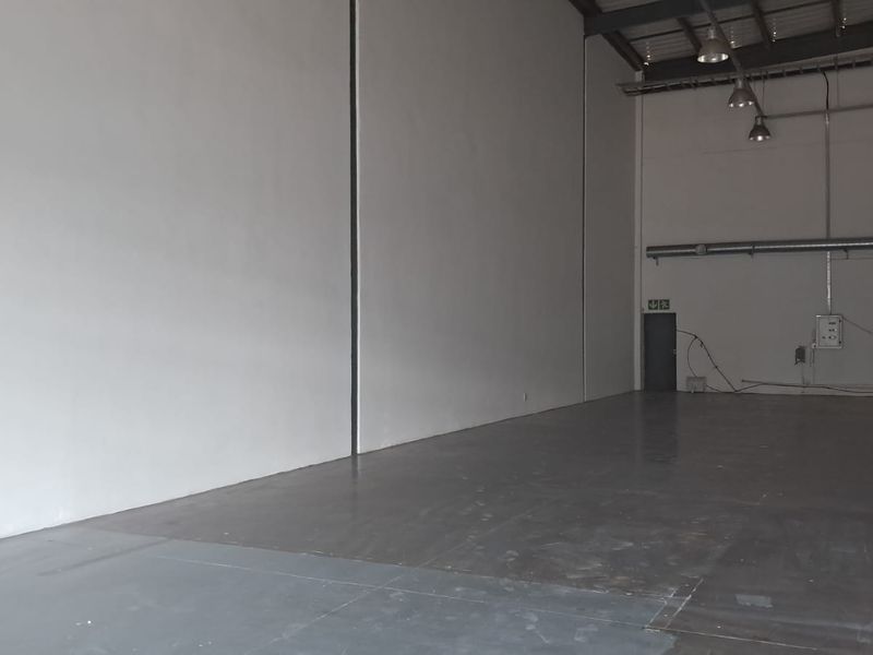 Spacious industrial warehouse unit featuring high ceilings with exposed steel trusses, industrial lighting, and durable concrete flooring, suitable for various commercial or storage uses.