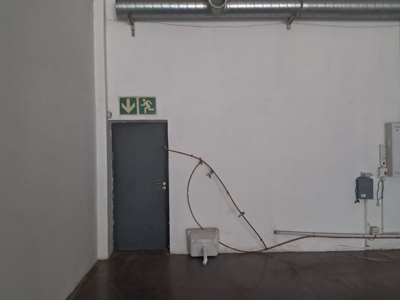 Industrial utility space featuring exposed ductwork, an electrical distribution board, and a utility sink with visible surface-mounted piping.