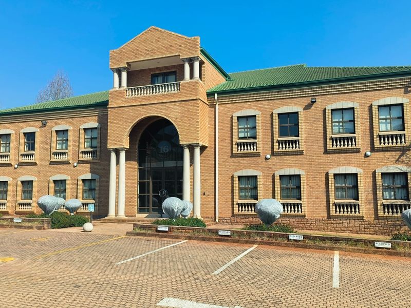 A professional front elevation of a two-story brick office building featuring a prominent arched entrance, balcony, and dedicated paved parking area.