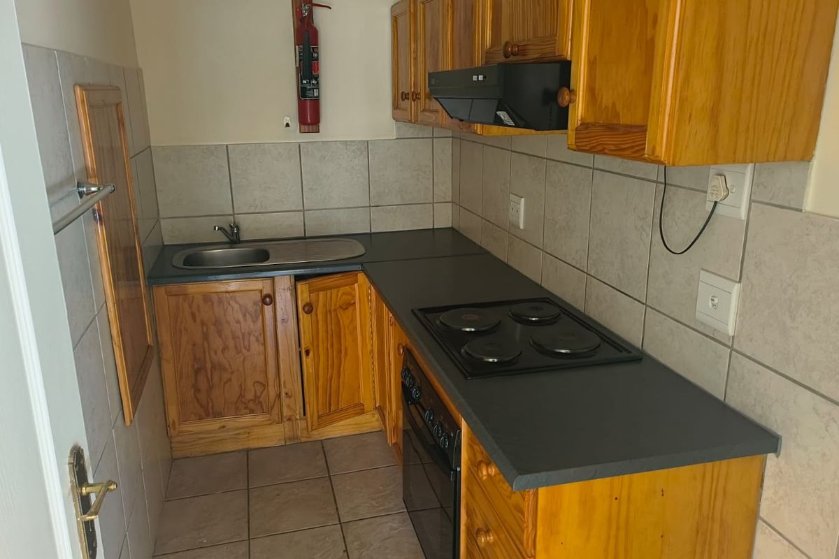 Compact office kitchenette featuring wooden cabinetry, dark laminate countertops, integrated electric hob, oven, and extractor fan with tiled backsplash and flooring.
