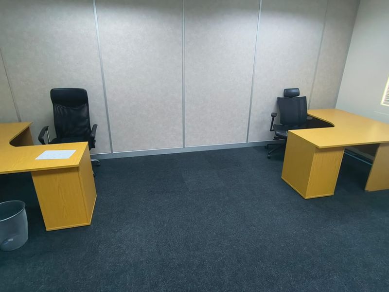 A functional office space featuring dark carpet flooring, modular wall panels, and natural light provided by a window with venetian blinds.