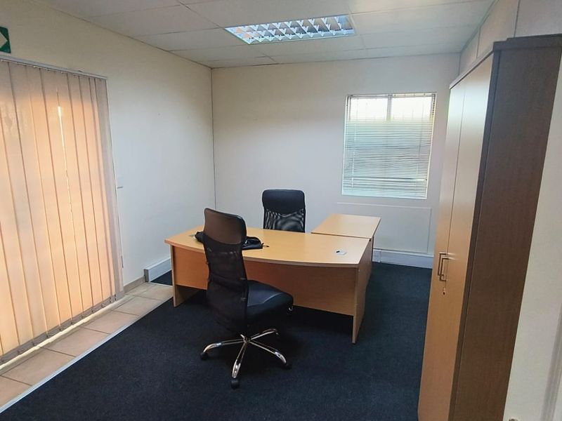 A functional office space featuring carpeted flooring, a suspended ceiling with recessed lighting, and dual window treatments for adjustable natural light.