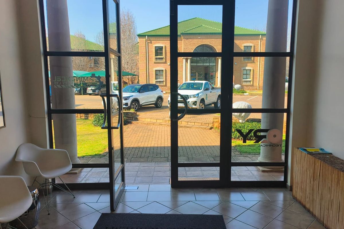 Bright office entrance featuring glass double doors, tiled flooring, and structural columns, providing a clear view of the exterior parking area.