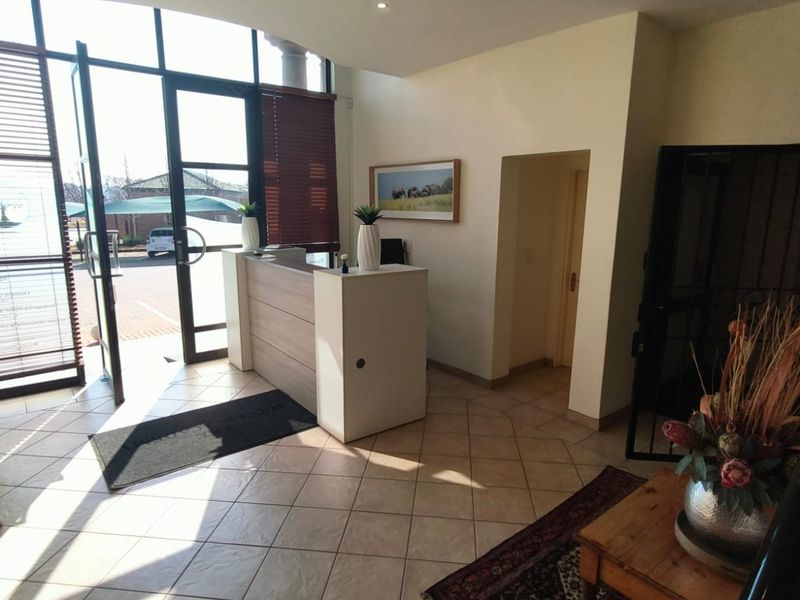 Bright office entrance area featuring a built-in reception desk, tiled flooring, and large glass doors providing ample natural light.