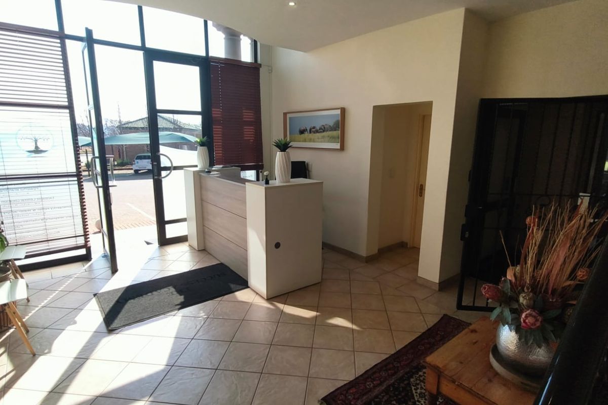 Bright office entrance area featuring a built-in reception desk, tiled flooring, and large glass doors providing ample natural light.
