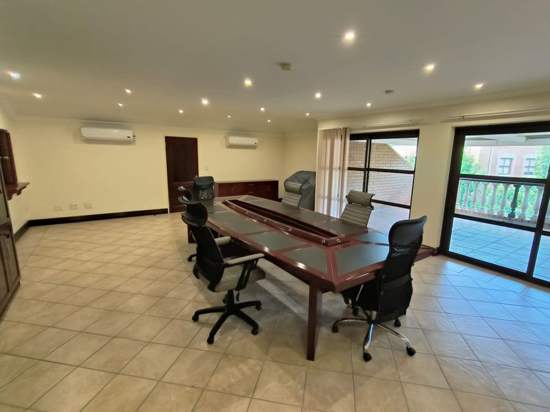 Spacious office area featuring tiled flooring, recessed lighting, dual split-system air conditioning units, and direct access to an outdoor balcony through sliding glass doors.