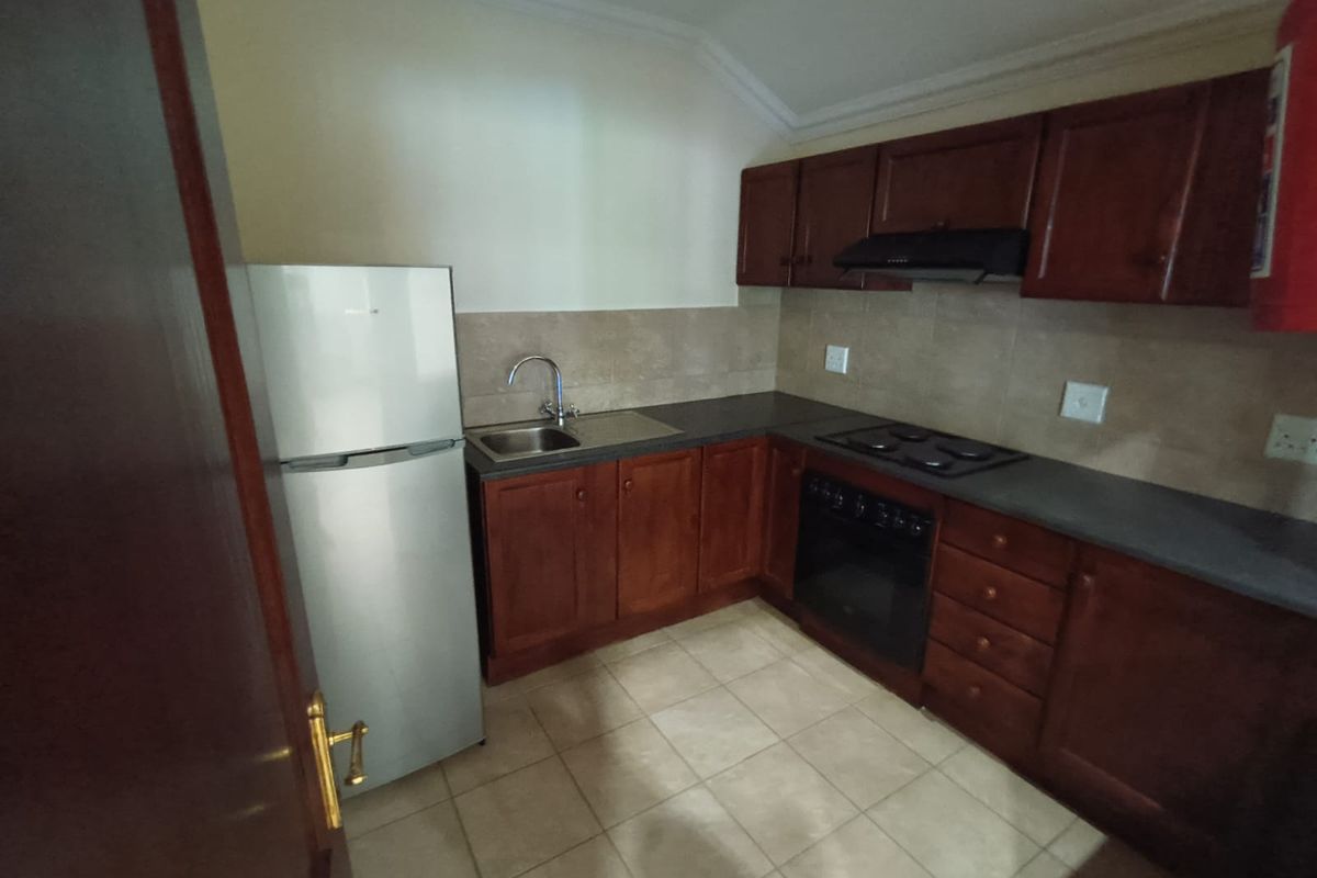 A compact office kitchen featuring dark wood cabinetry, a built-in oven, electric hob, extractor fan, and tiled finishes.
